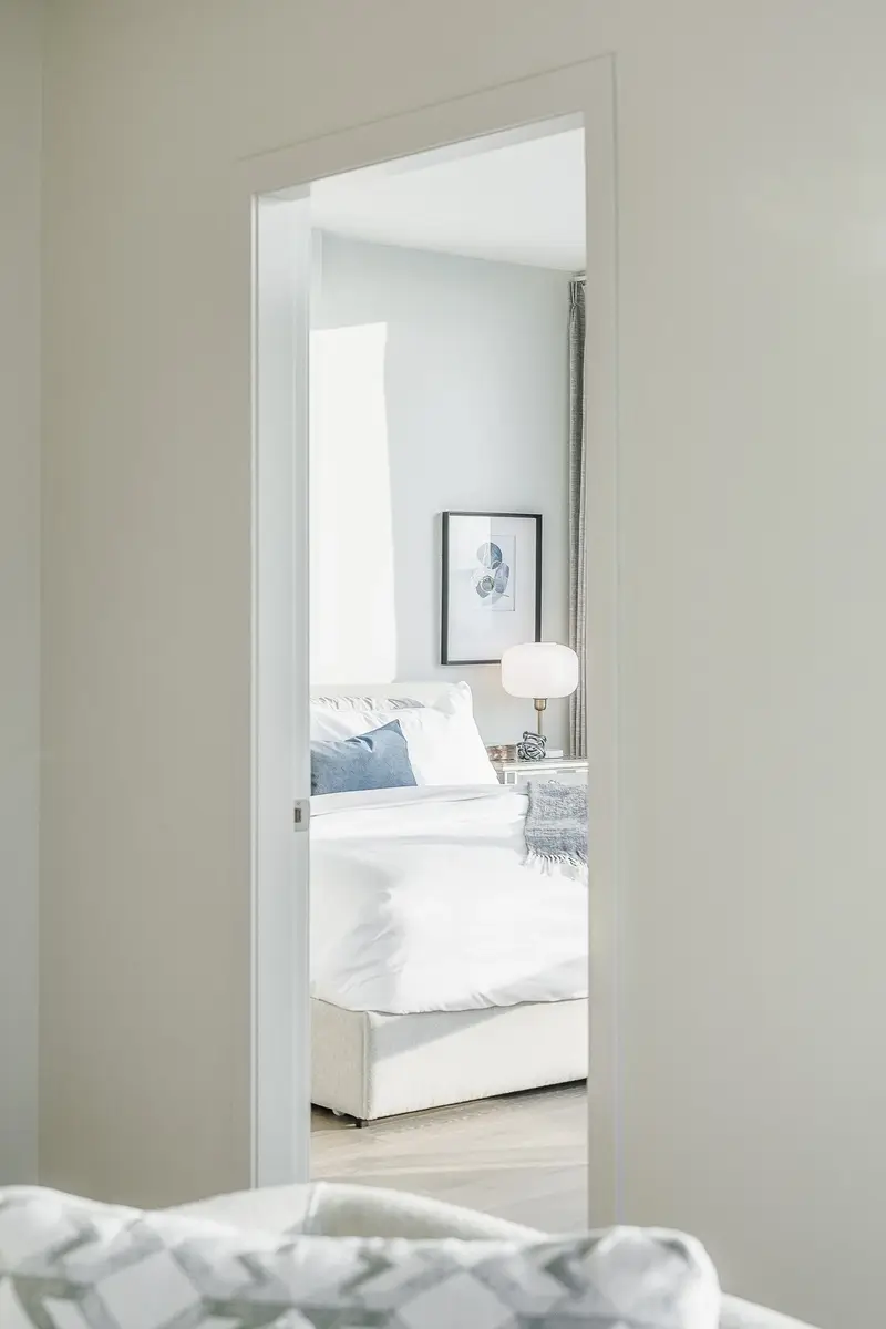 Through an open doorway to a made bed, a white globe lamp on the nightstand