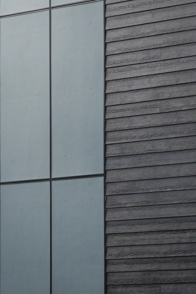 Cladding detail, a flat grey panel meeting dark board siding with a deep grain