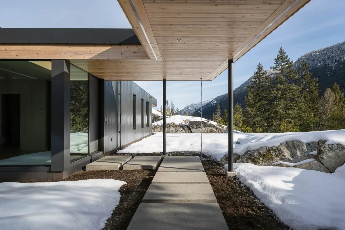 Warbler Residence, Whistler, covered entry walk under a pale wood soffit, snow and mountains beyond