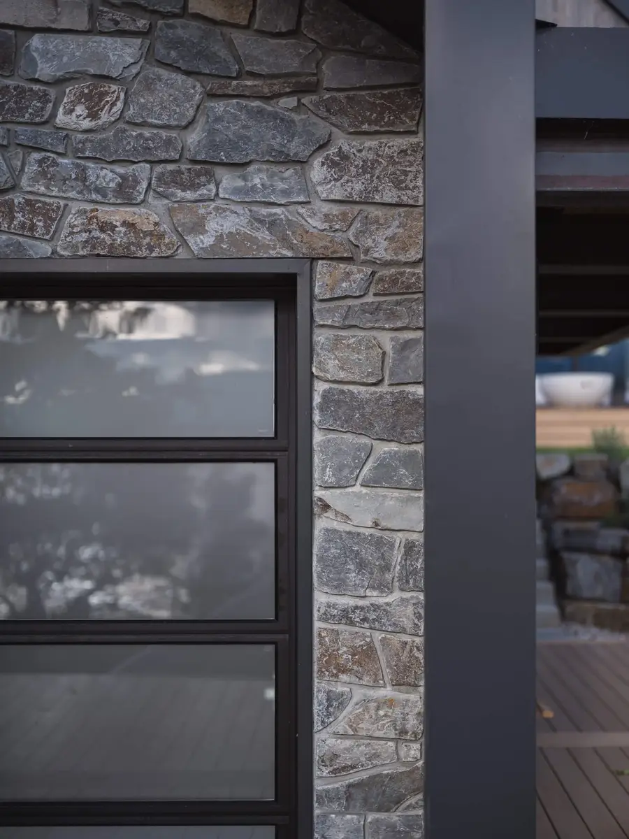 Rough stone wall meeting a dark metal post beside a glazed door