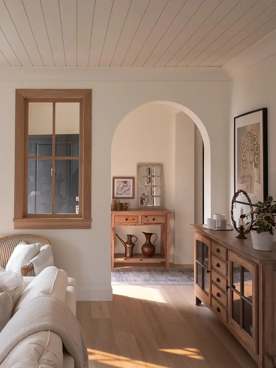 Living room past a wood framed interior window and through an arch to a console