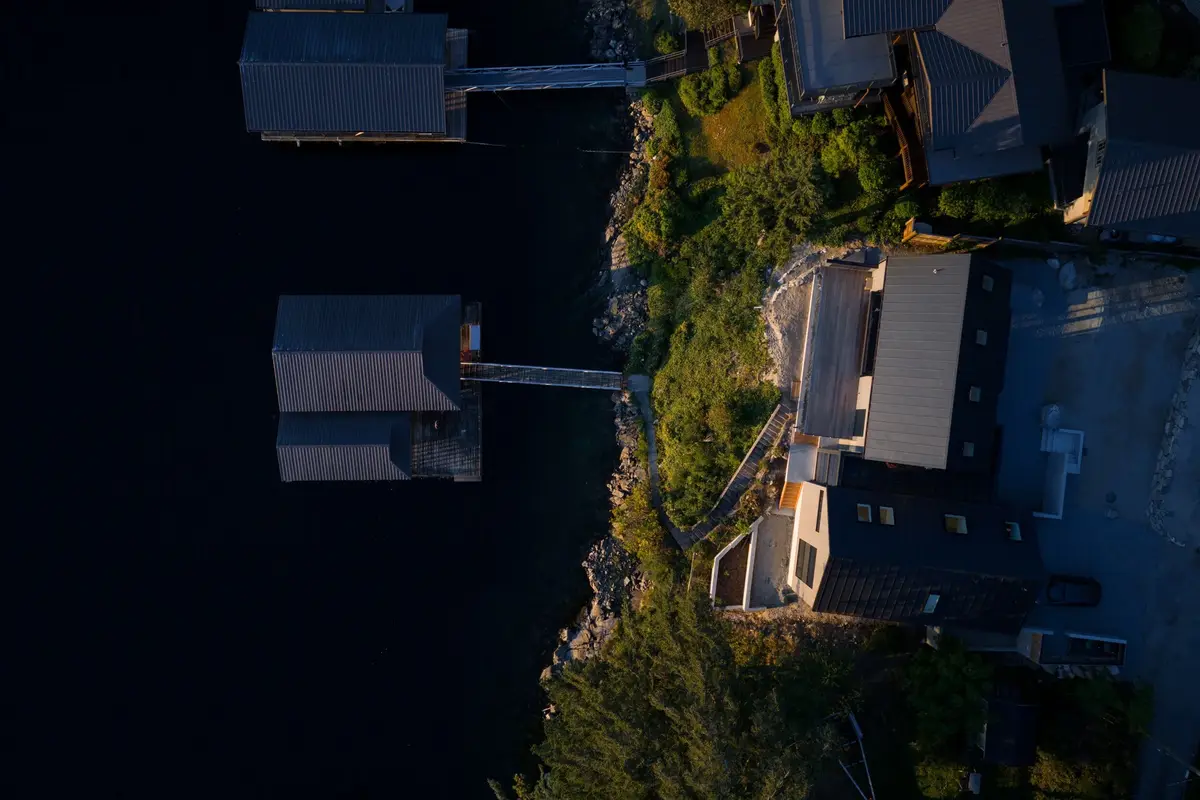 Straight down over the shoreline at sunset, dock roofs and rock along dark water