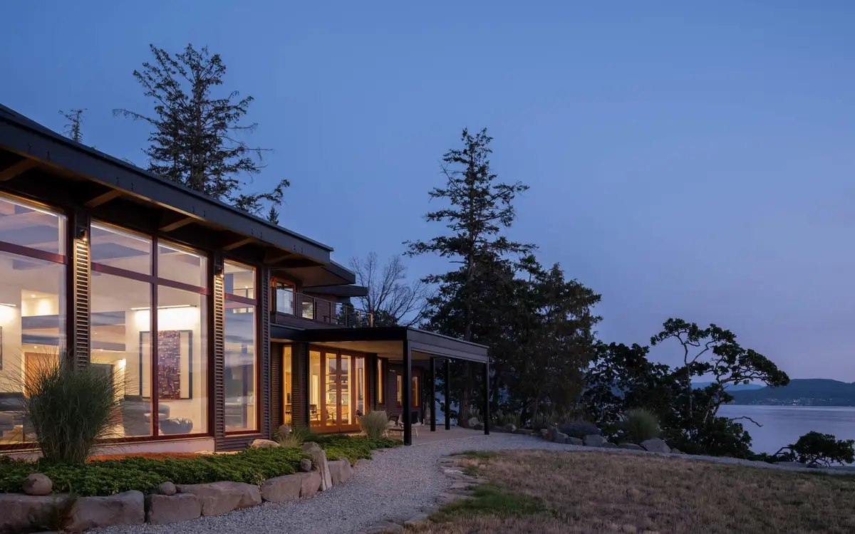 Blue hour along the glazed living volume, the lit room reading through the glass