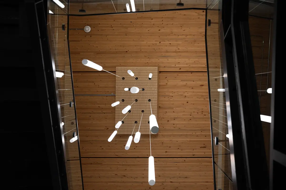 Cluster of tube pendants against the wood plank ceiling, seen past dark framed glass