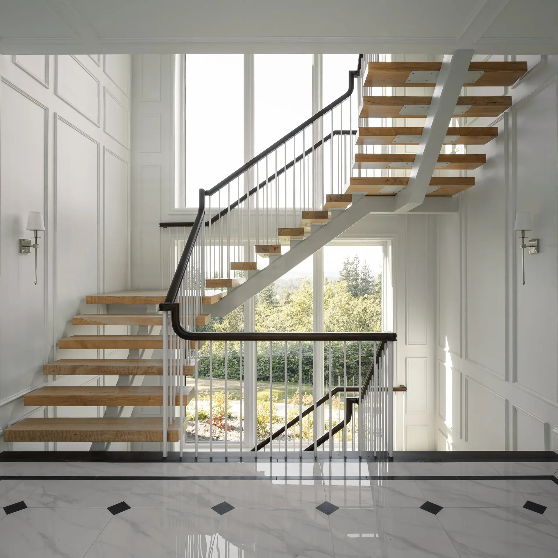 Open stair with wood treads against a two storey window looking out to trees and hills