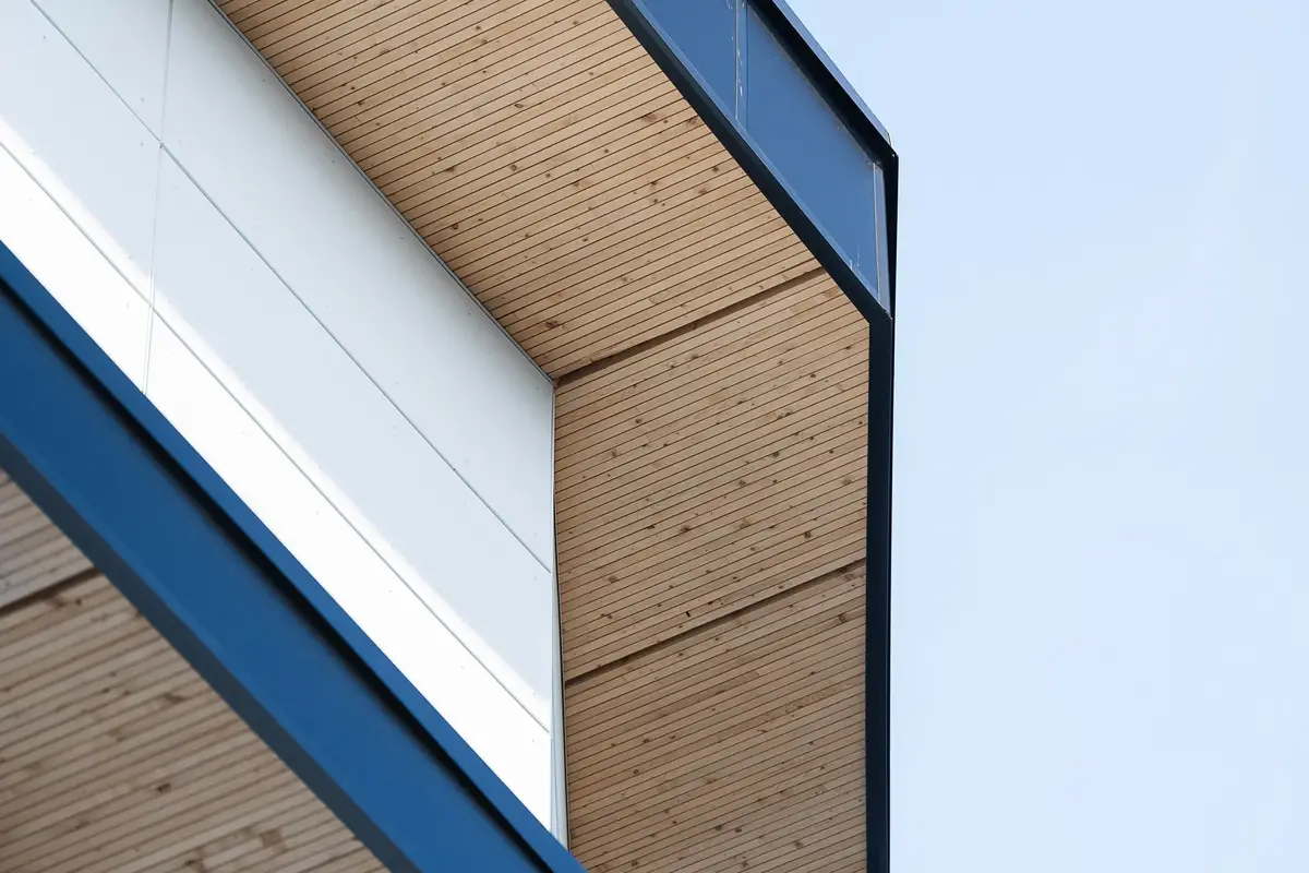 Roof edge from below, a dark fascia over wood soffit boards meeting a white panel wall