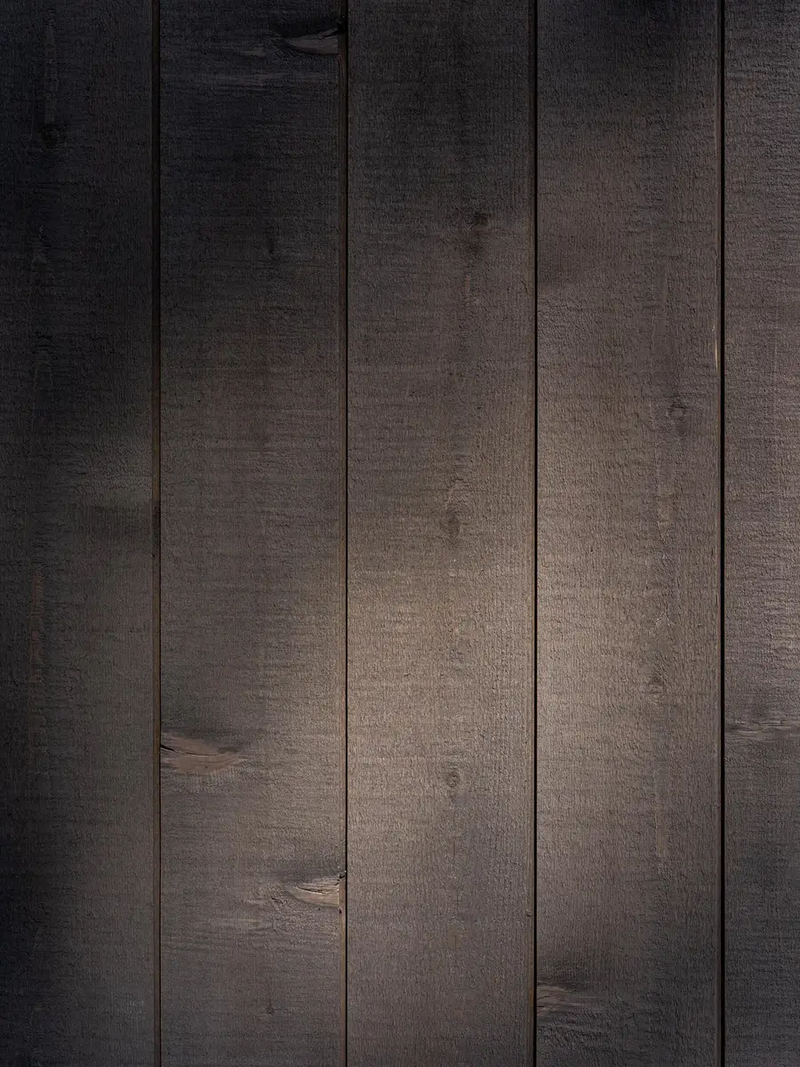 Close on dark vertical boards, saw marks and knots raking across the face