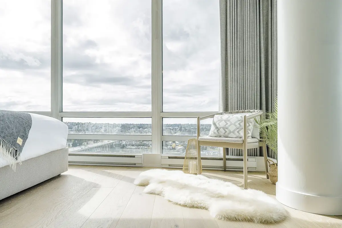 Open living and dining rooms behind corner glazing, a marina and the water far below