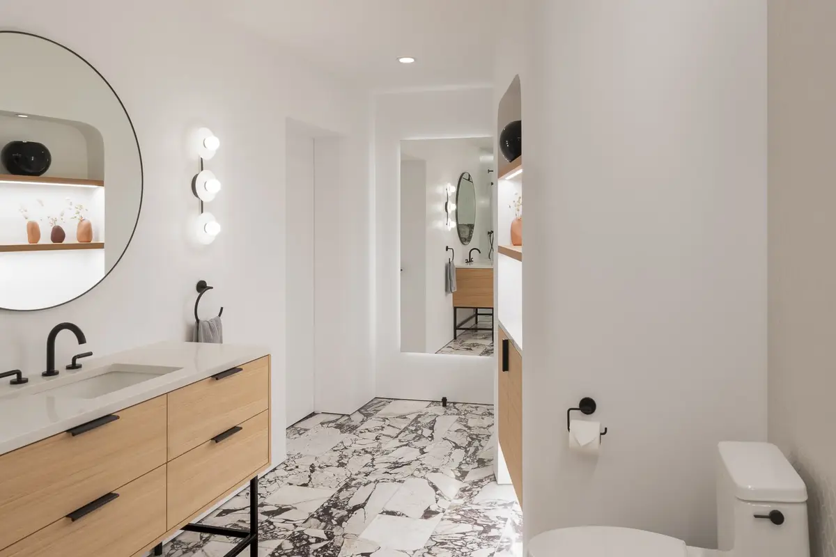 Bathroom vanity with a round mirror and wood drawers above a veined stone floor