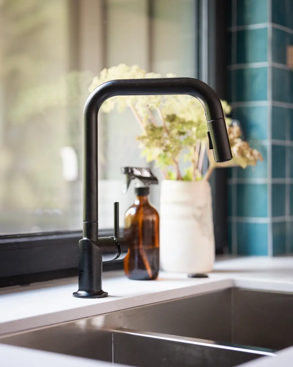 Black pull down tap over a stainless sink, blue green tile blurred behind