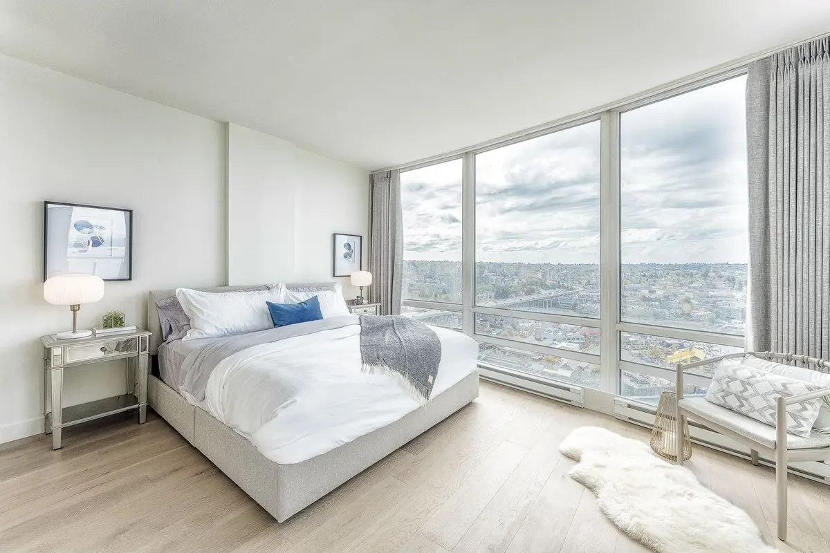 Bedroom wrapped in glass on two sides, the city spread out beyond the bed