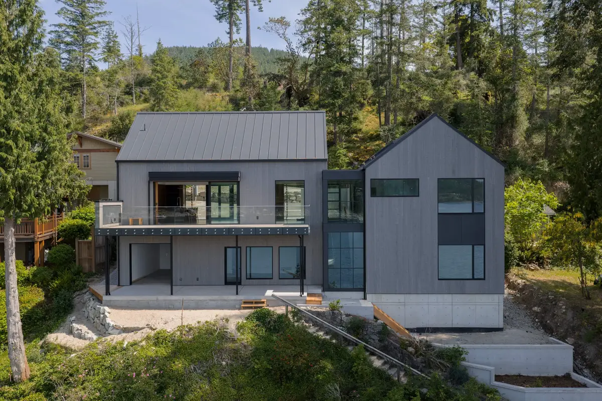 Two grey gabled volumes joined by a glazed link, set on a concrete base above the shore