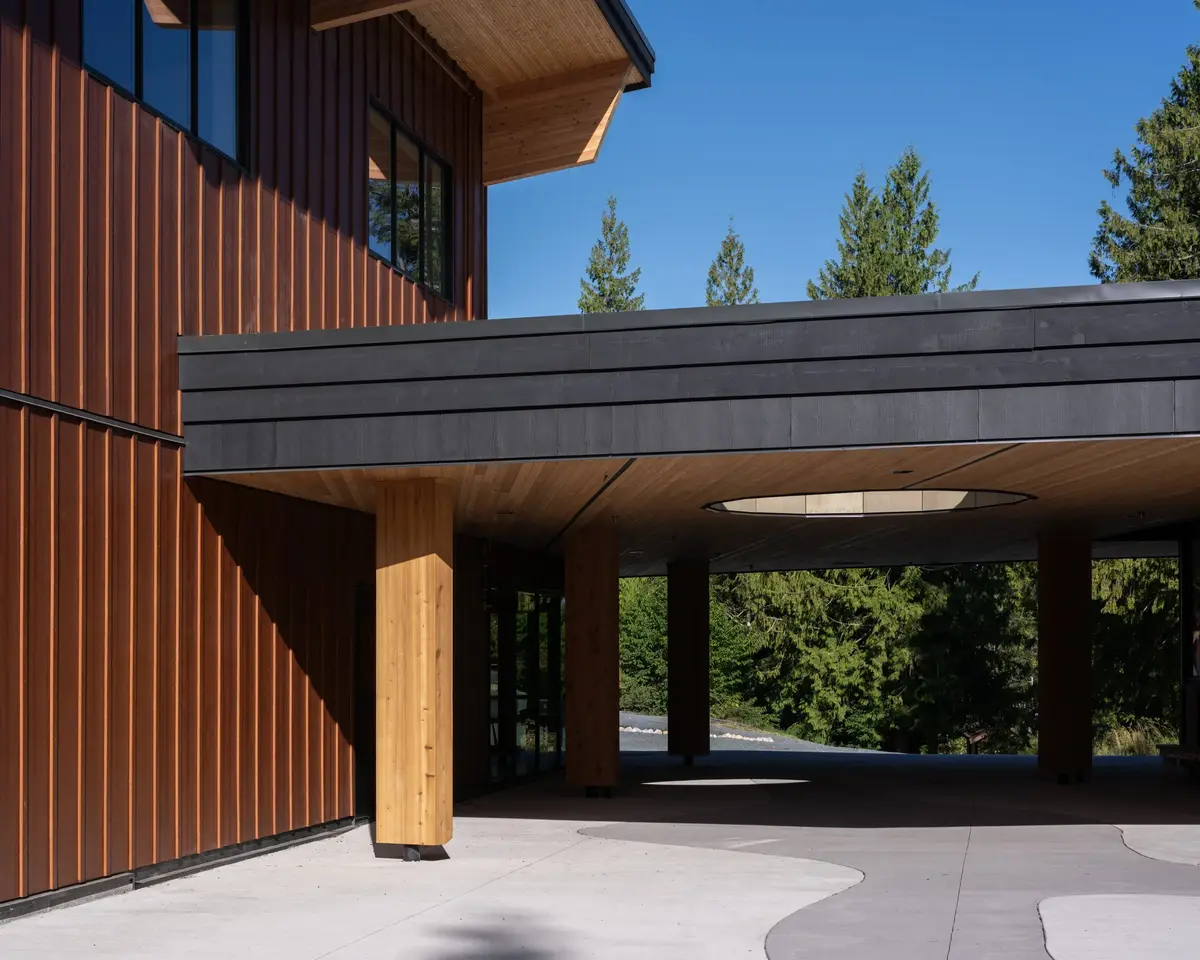 A dark canopy projecting from the wall over the covered walk, conifers behind