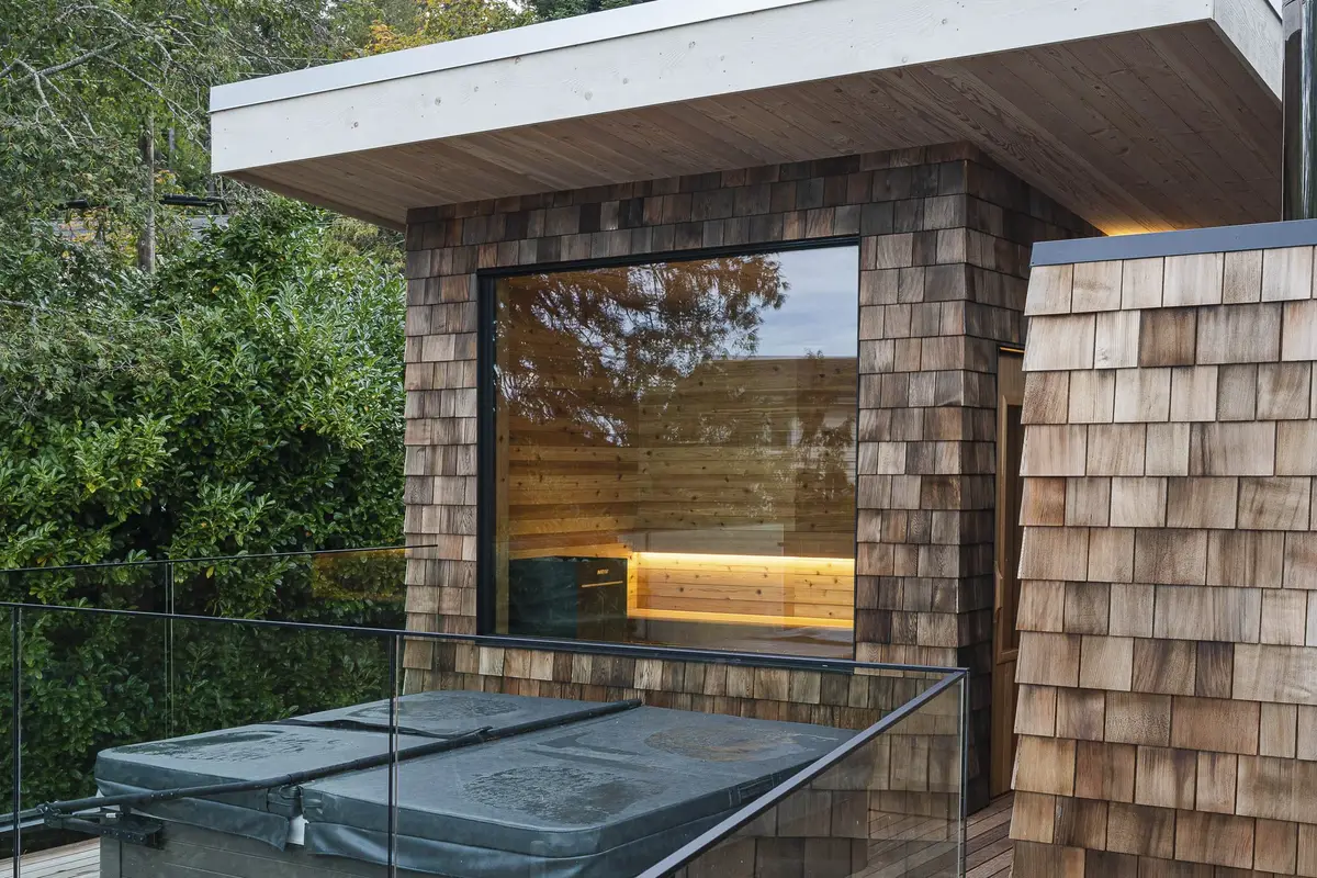 Rooftop terrace with a covered hot tub behind glass railing, sauna window lit within