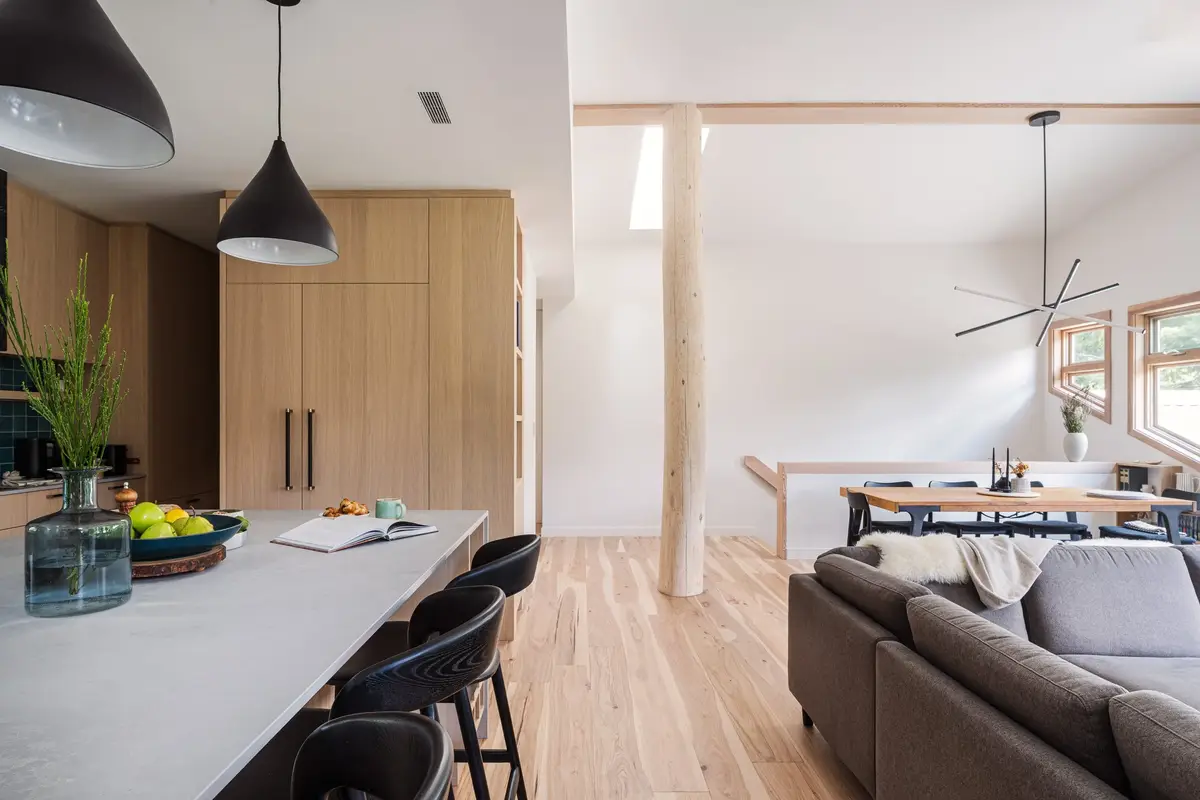 Looking past the island to the dining table and sofa, a peeled log post between