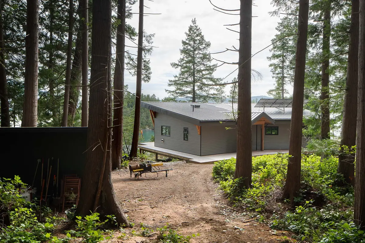 The house across a dirt clearing in the trees, a log splitter and tools nearby