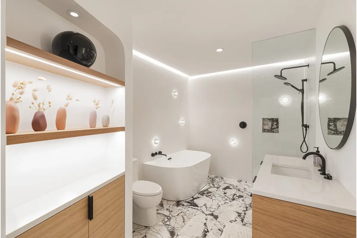 Bathroom with a freestanding tub, glass shower and a lit shelf of vases