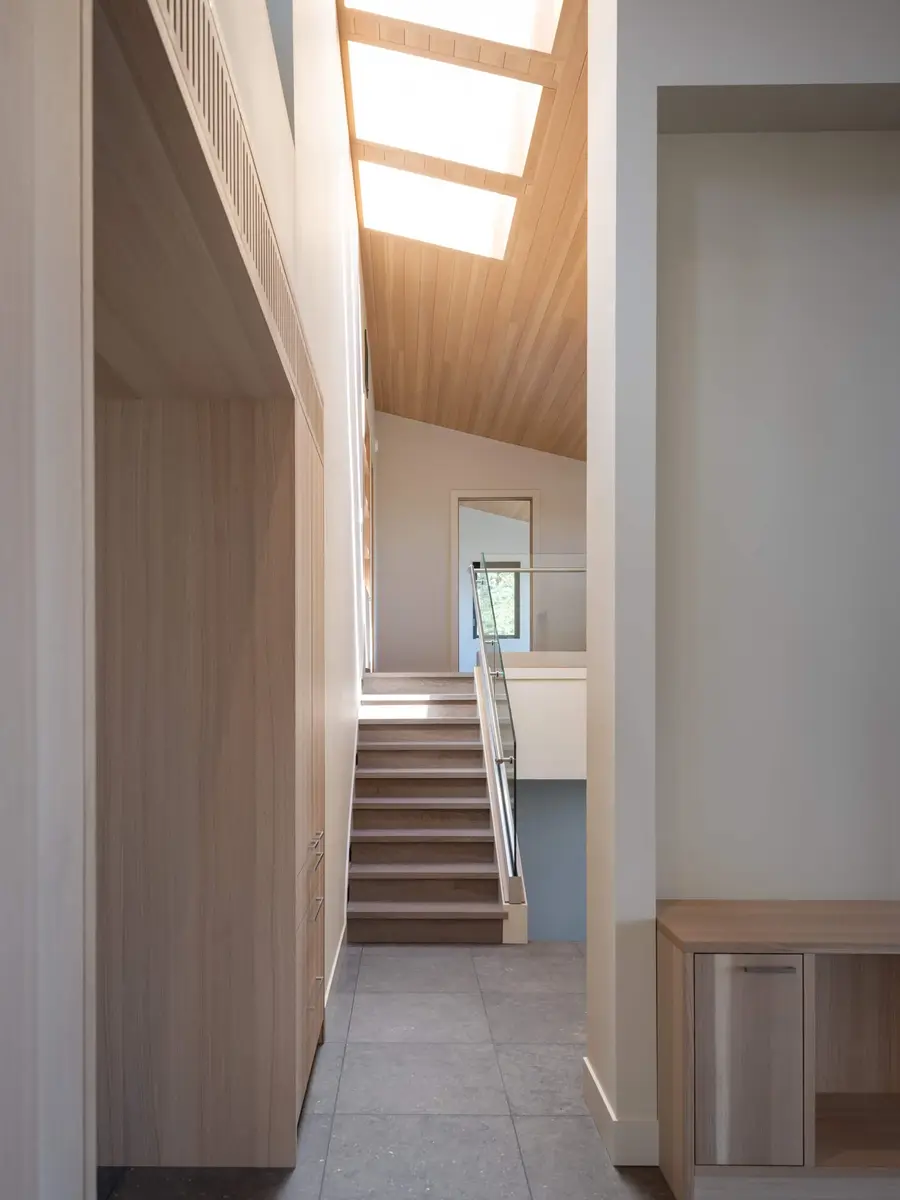 Stair rising at the end of a narrow hall, daylight dropping from a skylight above
