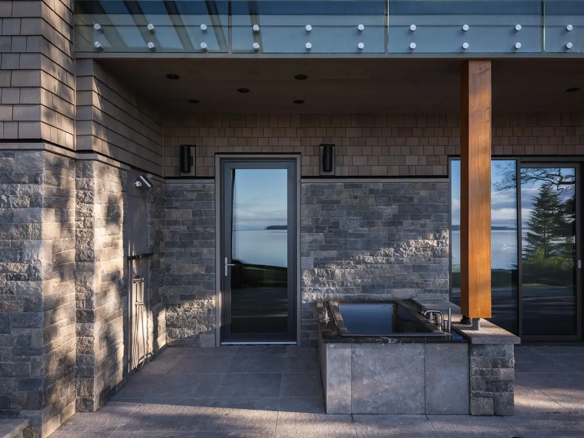 Outdoor soaking tub in a stone surround under a glass canopy, the water beyond
