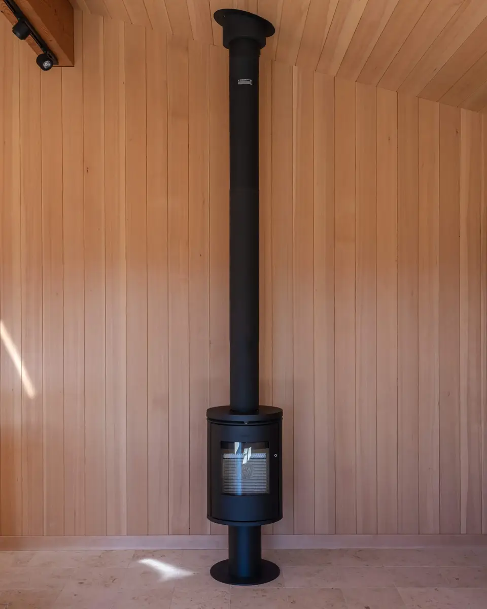 Black wood stove and its tall flue standing against a wood panelled wall