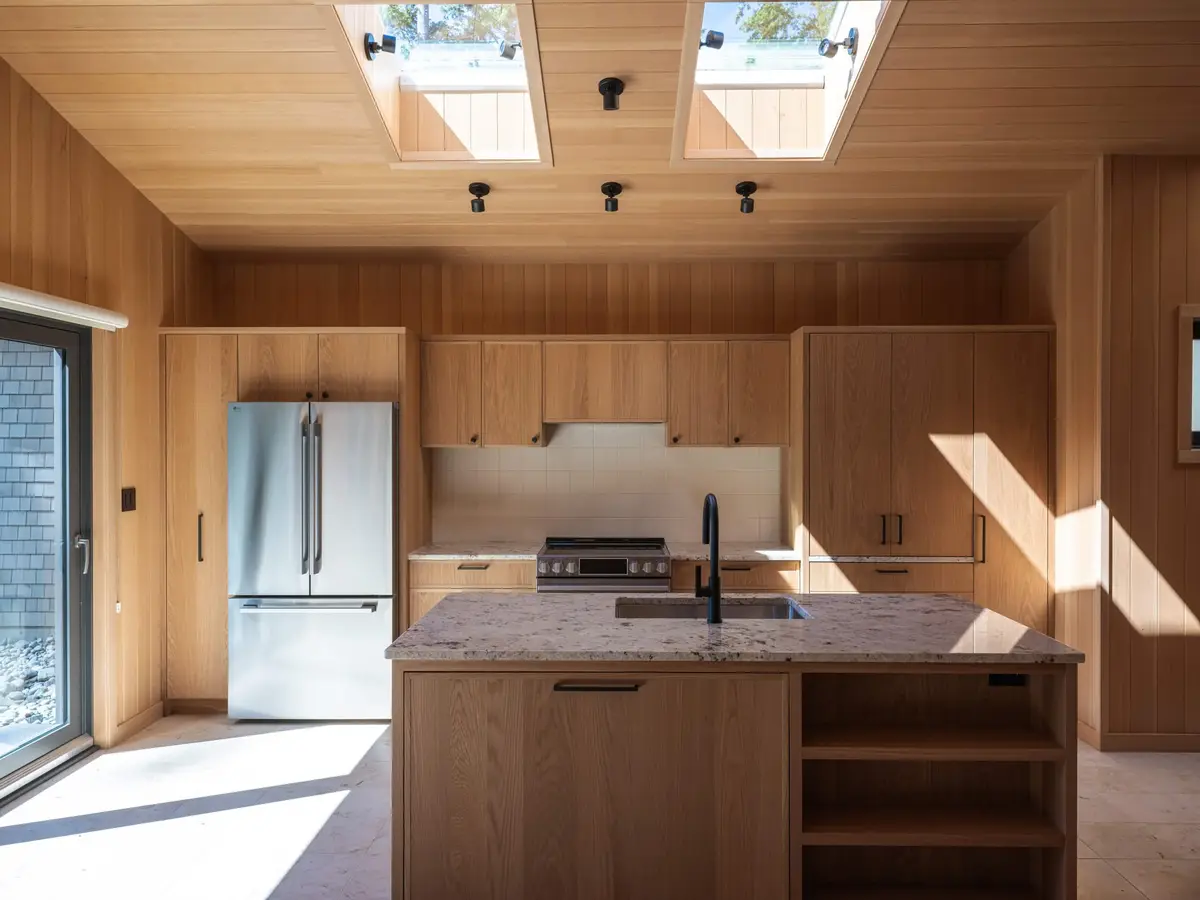 Kitchen lined in wood under skylights, a stone topped island with a sink and tall fridge