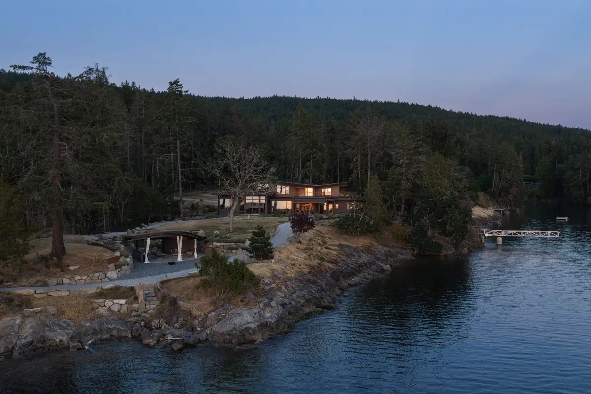 Dusk from above, the lit house and its dock on the forested point