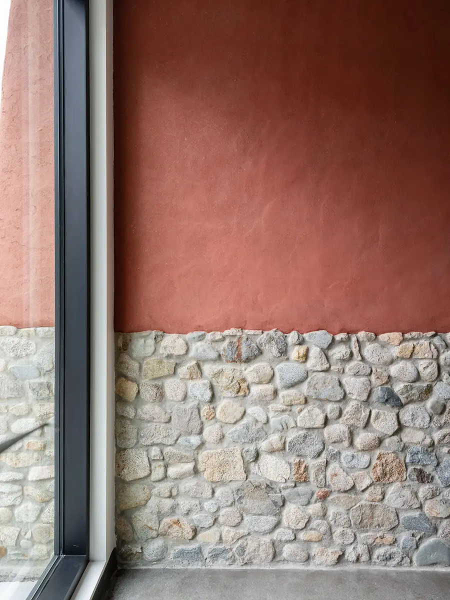 Earth red wall meeting rounded stone at the glazing, the two surfaces in one plane