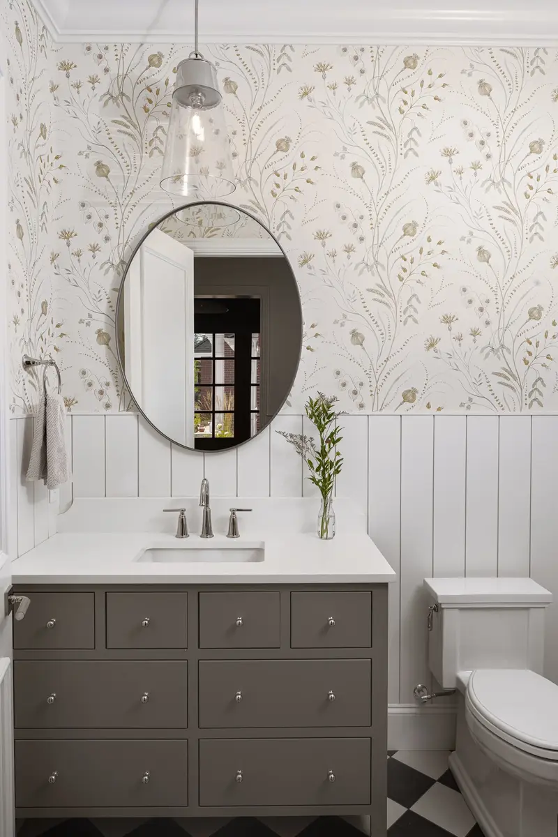 Powder room with floral wallpaper above white boarding, an oval mirror over a taupe vanity