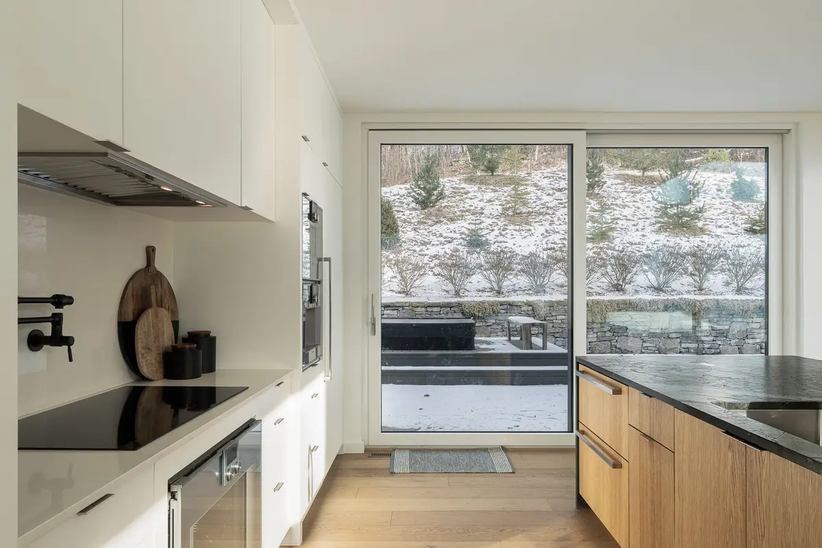 Cooktop run with wood boards and a black pot filler, sliding door to a snowy terrace