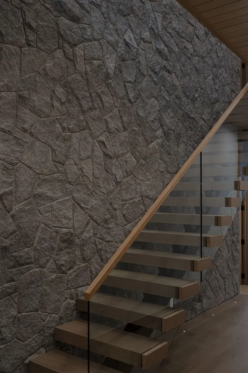 Stair rising beside a rough stone wall, glass balustrade and a slim handrail