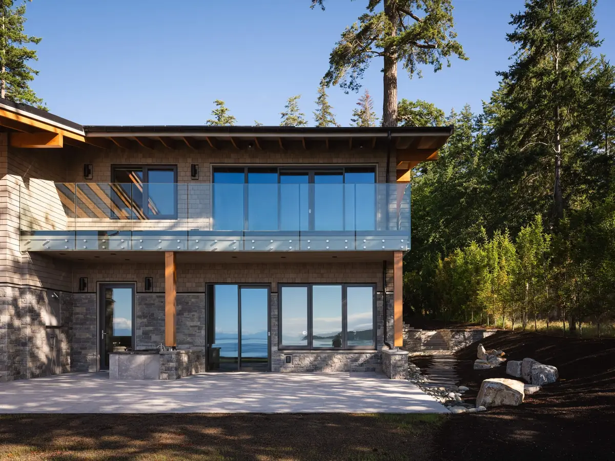 Two storey elevation with a glass railed balcony, tall trees close against the wall