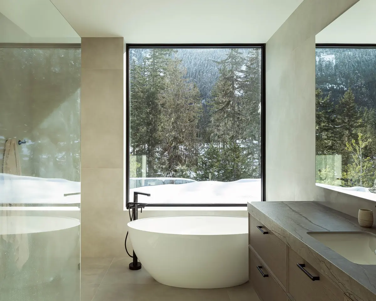 Bathroom with a freestanding tub at a corner window looking into forest