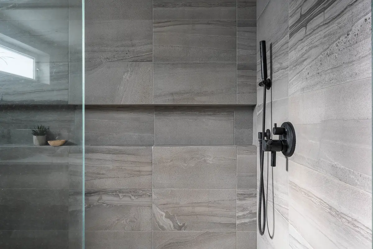 Shower wall in large veined tile, black fittings and a niche holding a small plant
