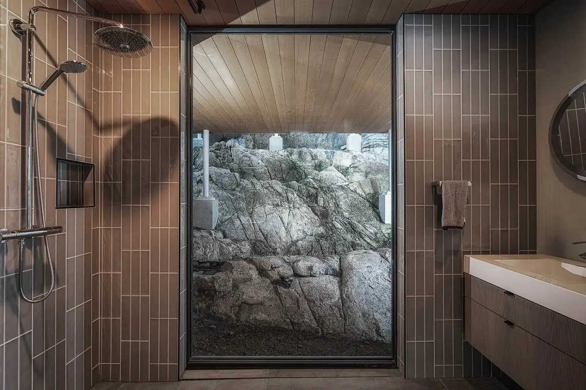 Shower in narrow tile with a glass door onto the rock face, vanity at right