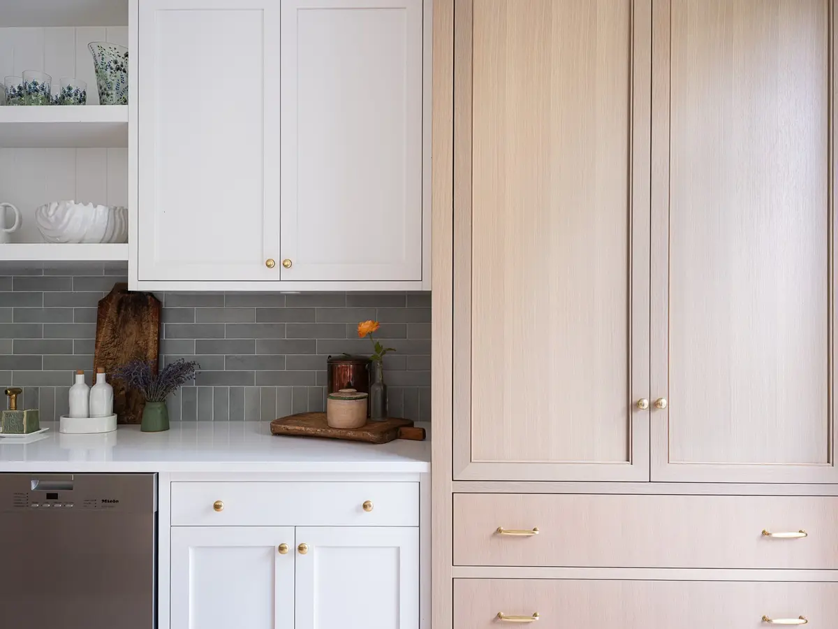 Tall pale wood cabinet beside white cabinetry, a dishwasher and green tile at left