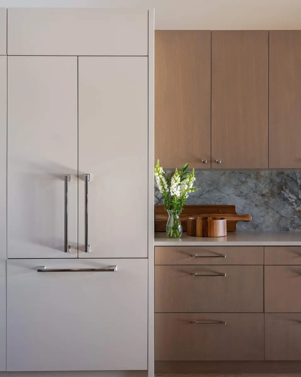 Panelled refrigerator next to pale cabinetry, flowers and wooden boards on the counter below