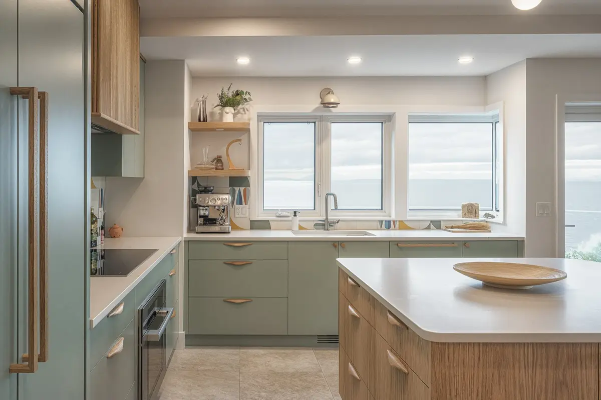 Kitchen windows above the sink looking out to the water, green cabinets and a wood island