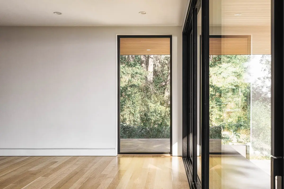 Unfurnished room with a pale wood floor and full height glazing onto the forest