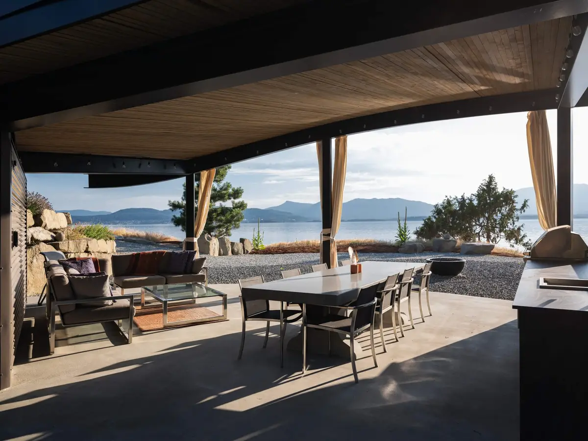 Under the pavilion roof, a long table and lounge chairs open to the water