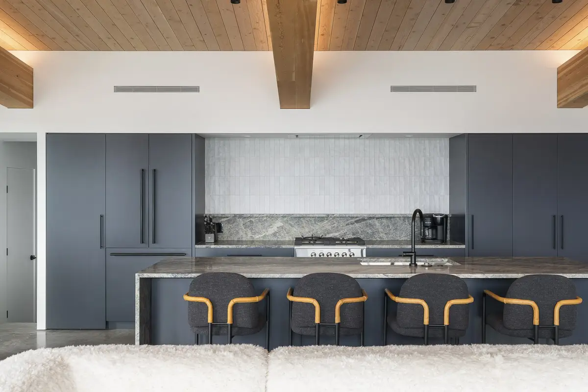 Kitchen island with four stools, range and a veined stone backsplash behind