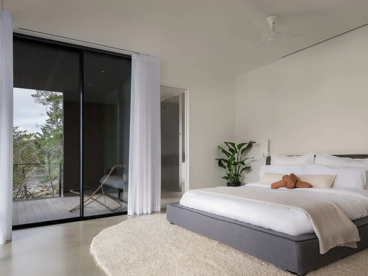 Bedroom with a low bed and sheer curtains, sliding glass to a deck and trees