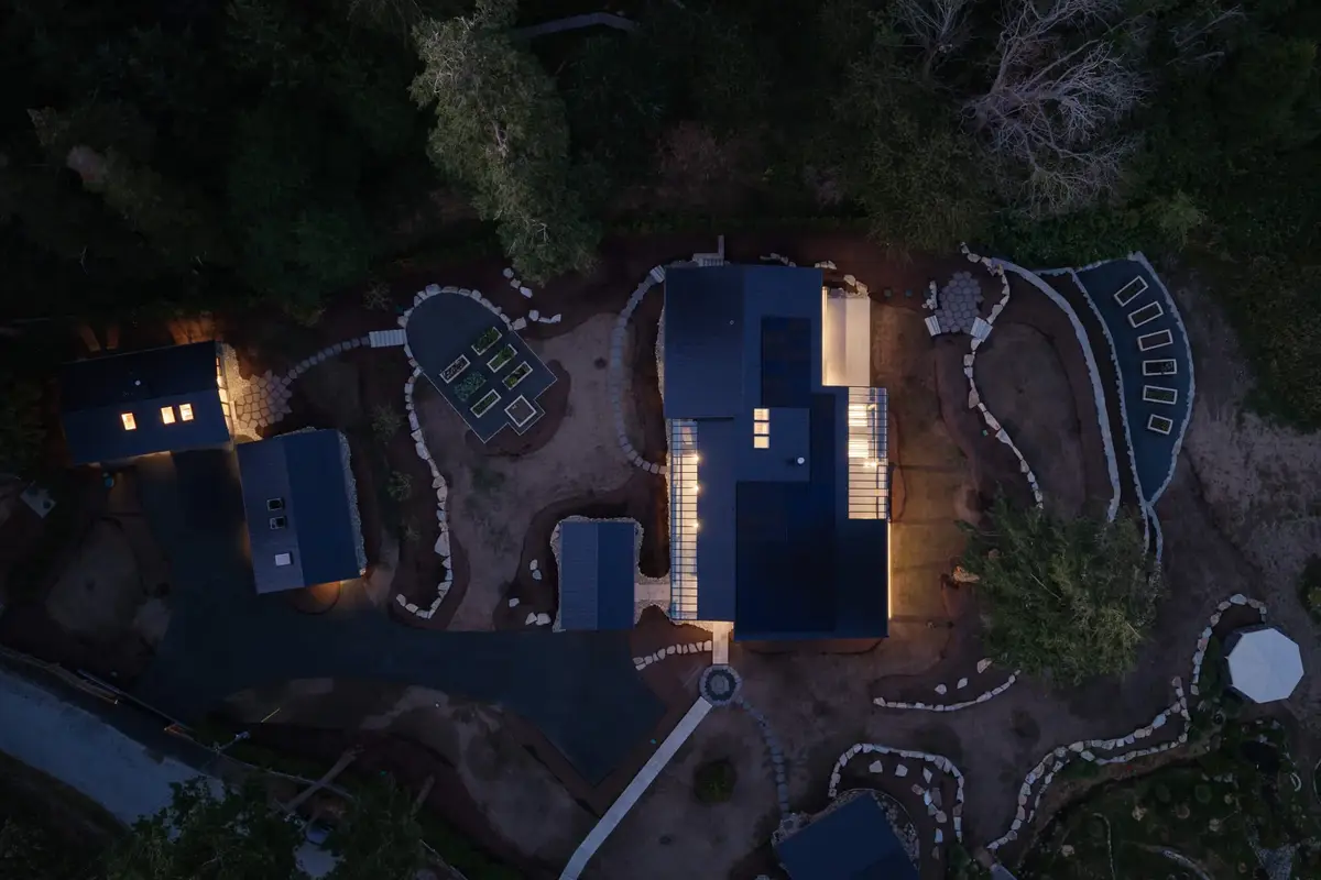 Directly overhead at twilight, dark roofs among the trees with terraced paths and beds around them