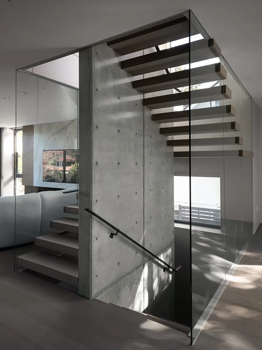 The stair against its concrete wall, glass balustrade and a slim black handrail