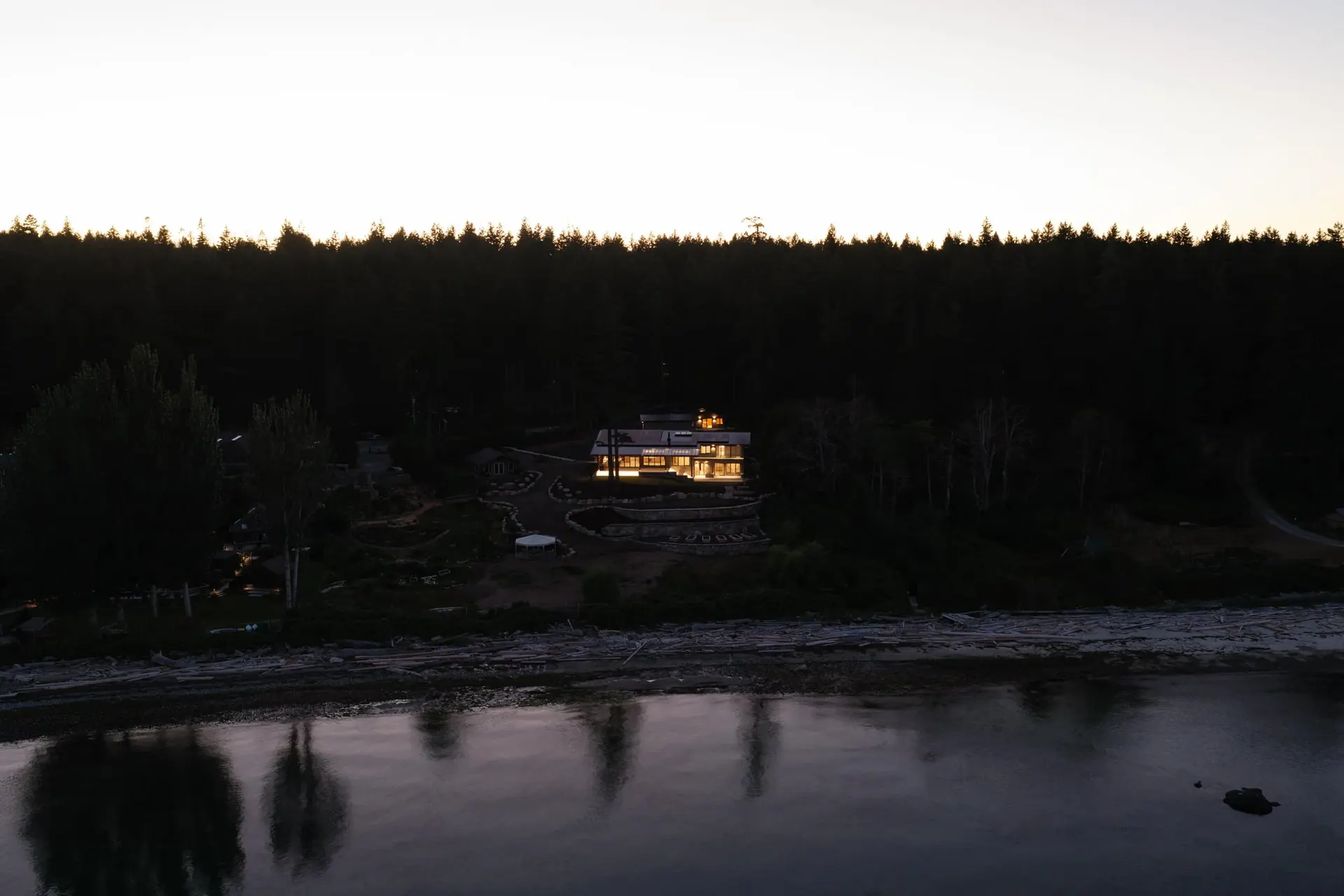 Seen from across the water at dusk, warm light in the trees along the shore