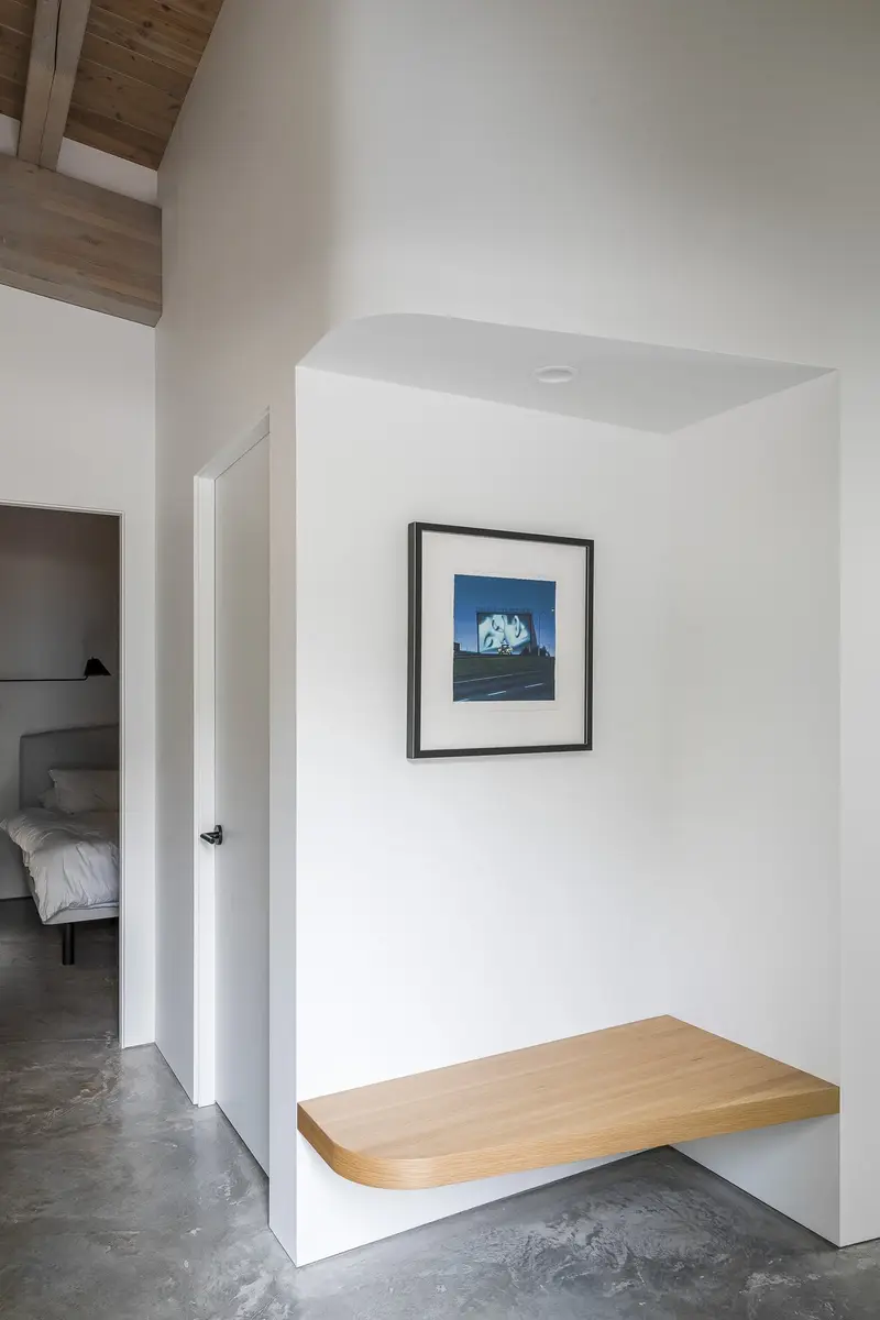 A floating wood bench in a niche below a framed picture, bedroom door beyond