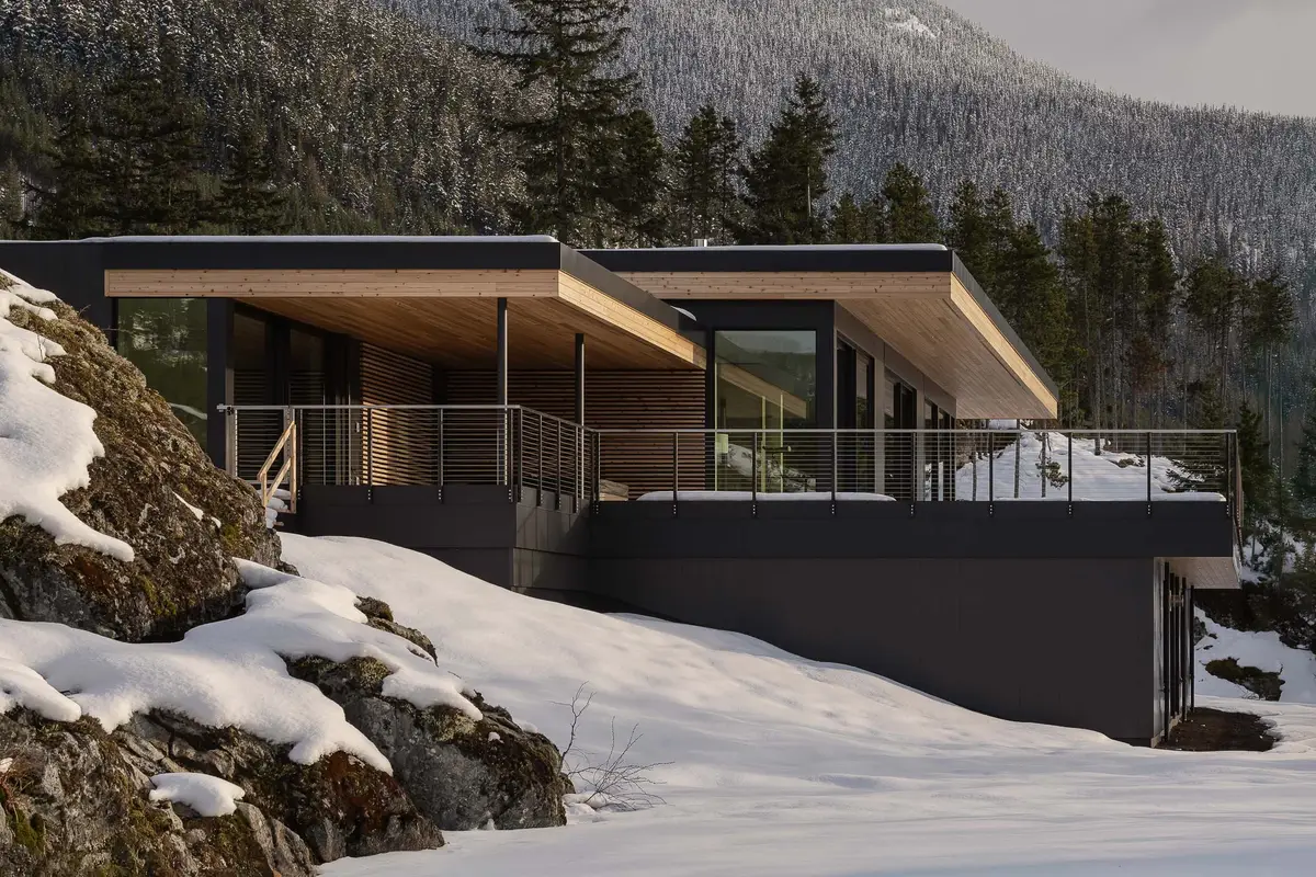 The house along a rock outcrop above the snow, a long dark volume under a pale wood soffit