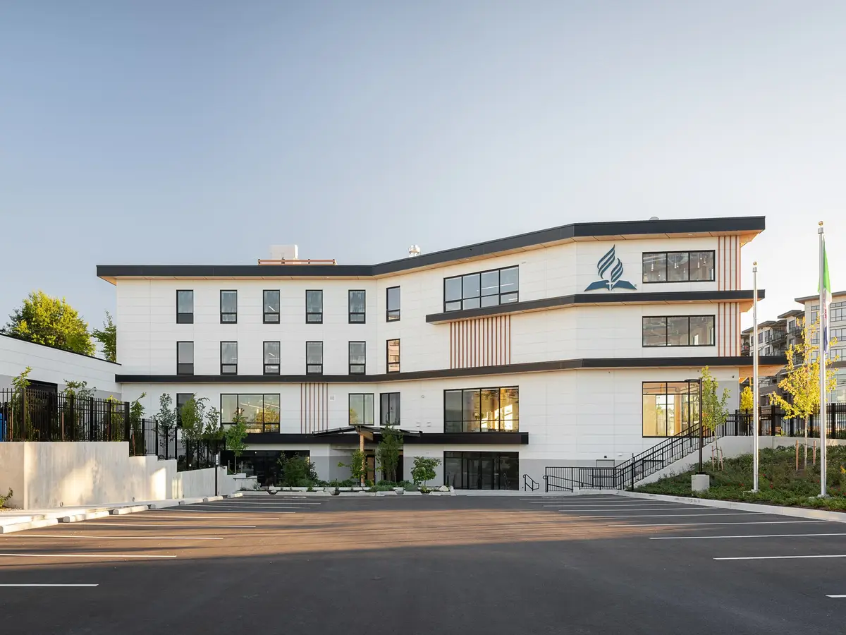 The full elevation seen across a parking lot in evening light, an emblem at the top floor