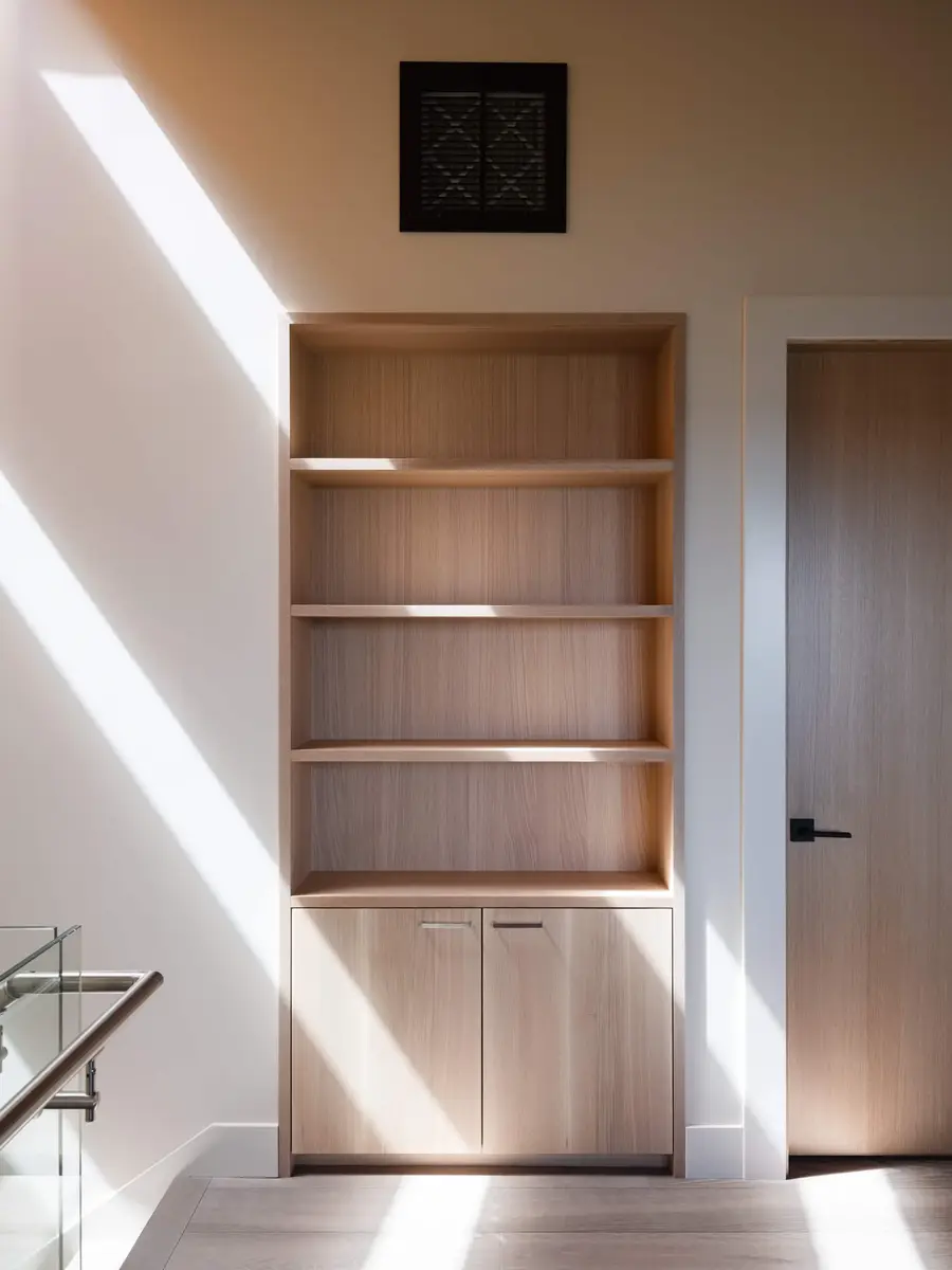 Built in bookcase in pale wood, hard sunlight falling across the empty shelves