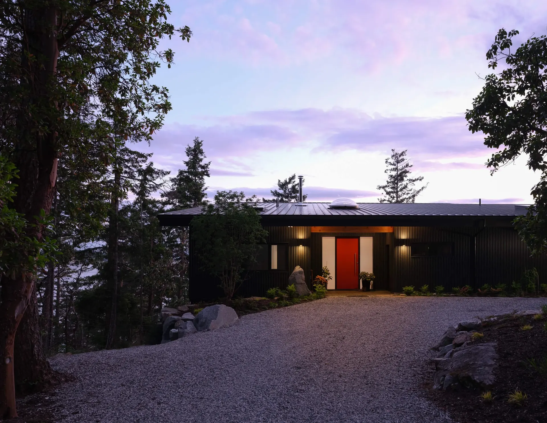 Dusk at the entry, wall lights along the dark facade and the red door glowing