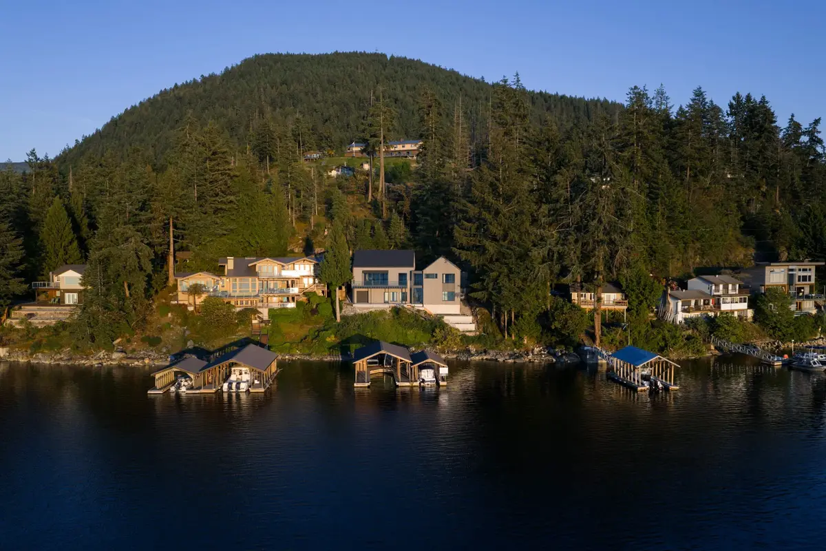 Houses and boathouses along a forested shoreline in low golden light, still water below